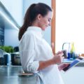 Young woman using tablet in kitchen at home and drinking coffee