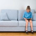 girl sitting on sofa playing game on tablet