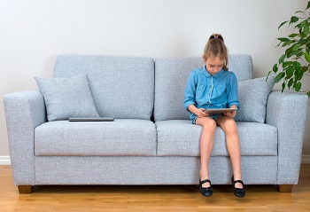 girl sitting on sofa playing game on tablet
