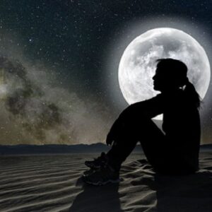 woman sitting on sand in the moonlight