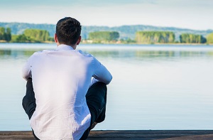 Man sitting alone by lake thinkinga