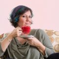 woman holding red coffee mug while relaxing in armchair